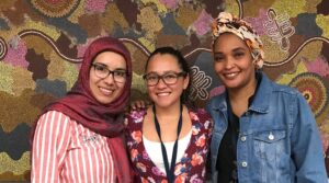Three doulas stand in front of patterned Aboriginal artwork.