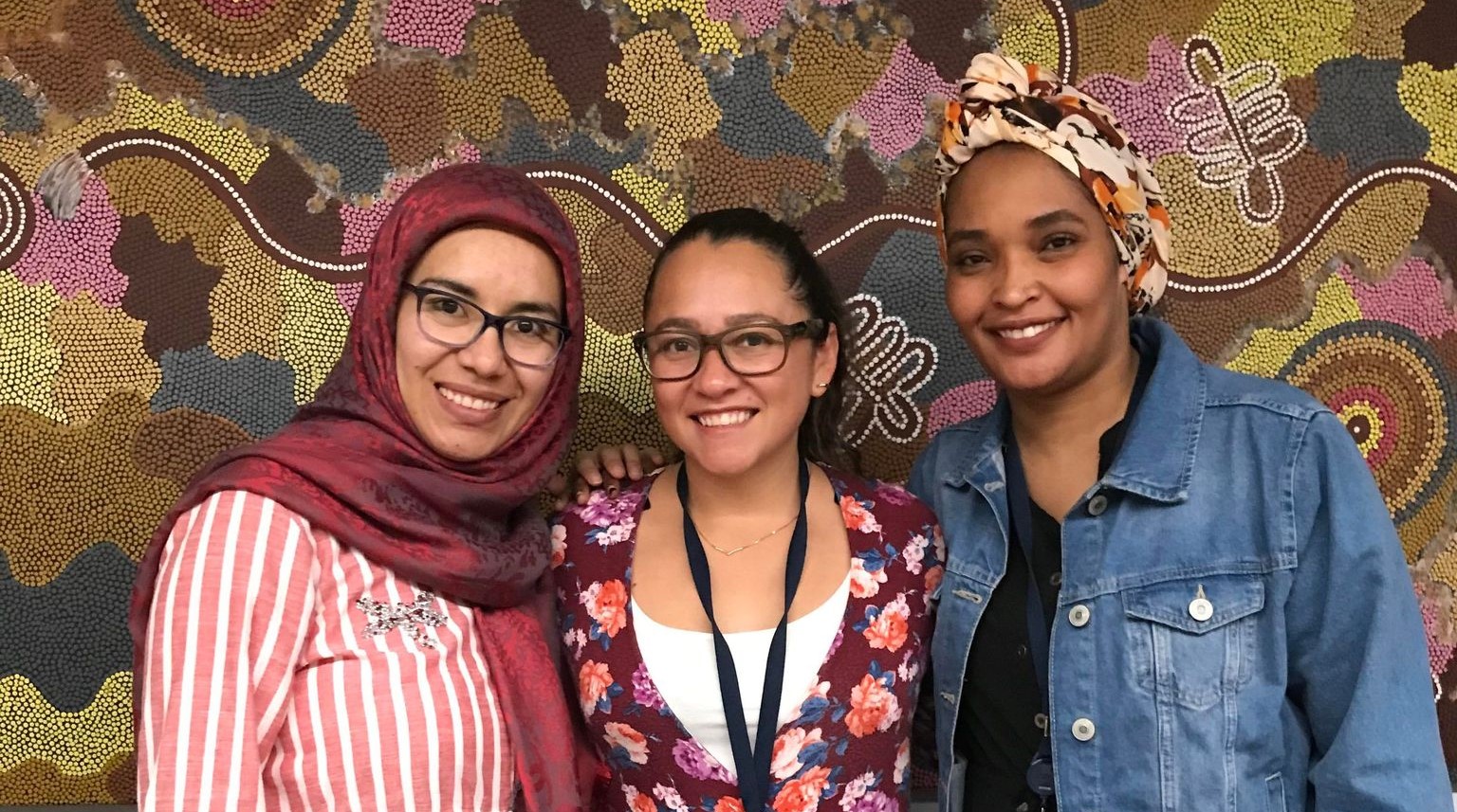 Three doulas stand in front of patterned Aboriginal artwork.